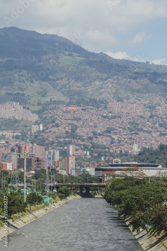 View of the river in Medellin, colombia on a sunny day. Visible a large amount of houses and slums in the background on the green hills.
