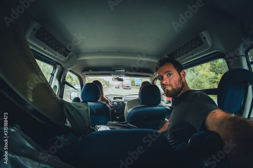 Three people riding in a minivan with loaded skis, going on a trip. One person is holding a camera and making a trip selfie. © Anze