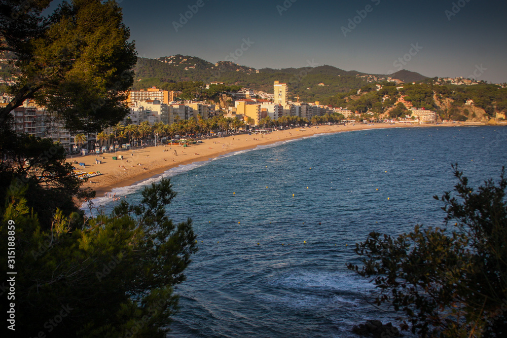 Panorama of beach in Tossa de Mar, close to Lloret de mar in Catalunya, Waves and sandy beach with city in the background are visible.