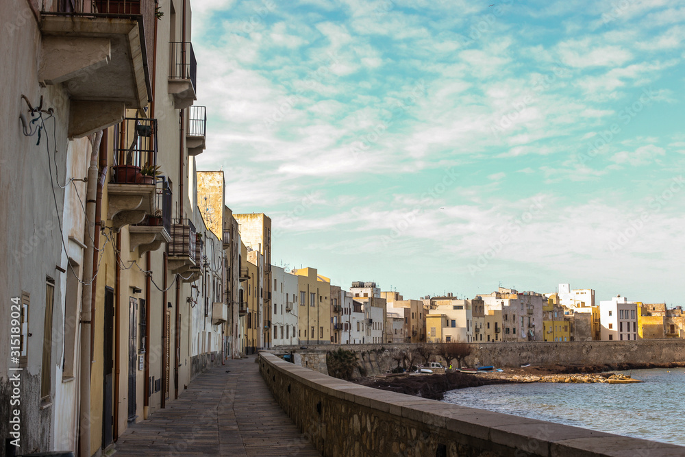Panoramic view of waterfront in Trapani, Italy. A row of houses next to the mediterranean sea in the city of Trapani on a sunny day with some clouds.