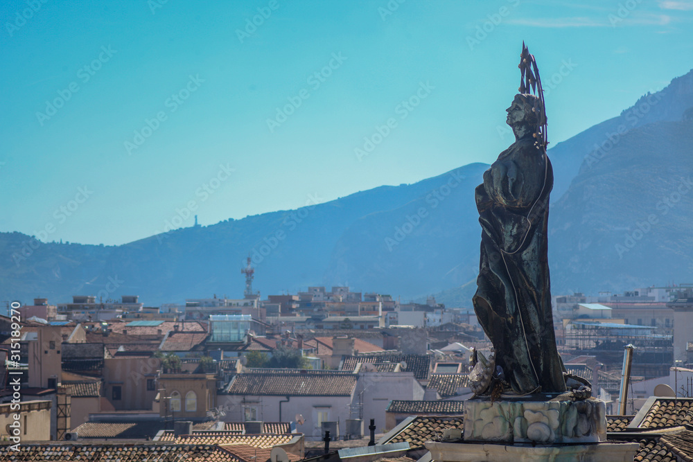 An angel on top of the Saint Dominic church in palermo, overlookng the city with some hills in the background.