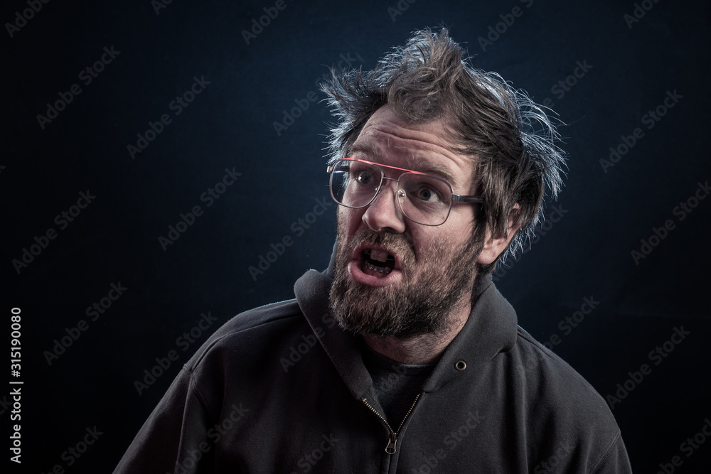 A goofy man with a beard, hipster glasses, rabbit teeth, dental braces on a dark red lit background with brown hoodie or sweater and electrified hair. A goofy man with a beard, hipster glasses, rabbit teeth, dental braces on a dark red lit background with brown hoodie or sweater and electrified hair.