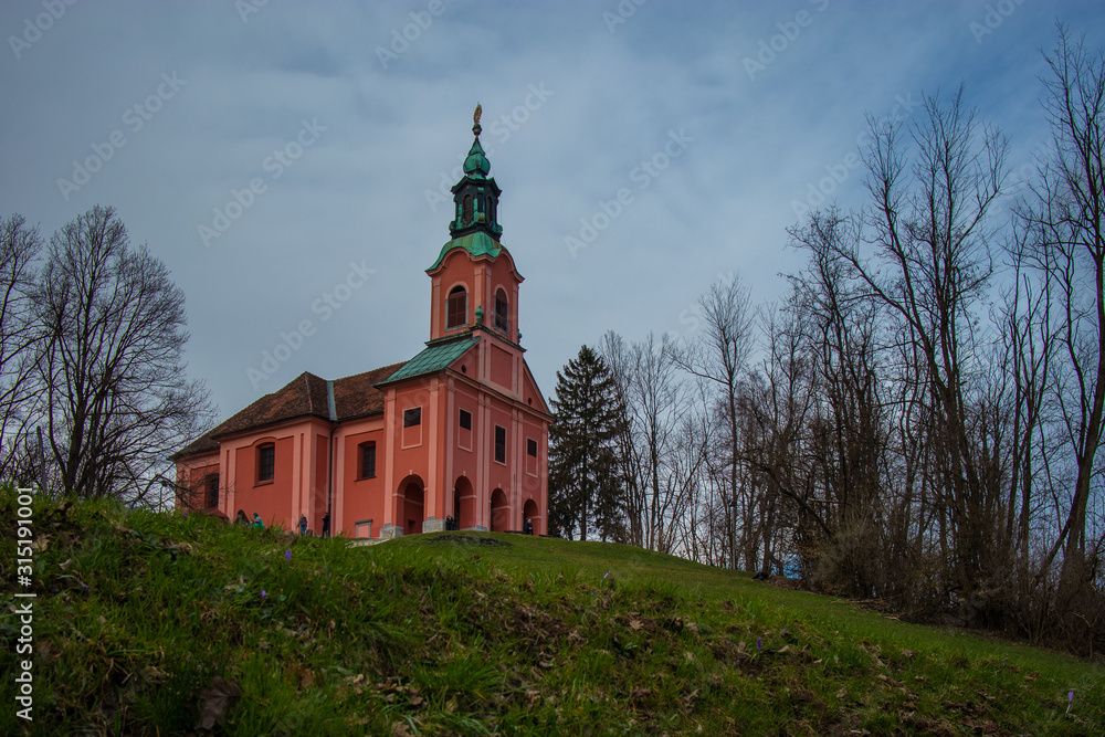 Red church with green copper roof on the top of the Roznik hill in Ljubljana slovenia on a cloudy day in early spring.