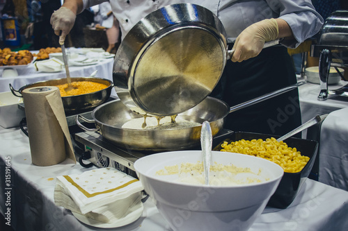 A professonal chef is pouring a sauce for pasta in a pan on electric stove on a banquet. photo