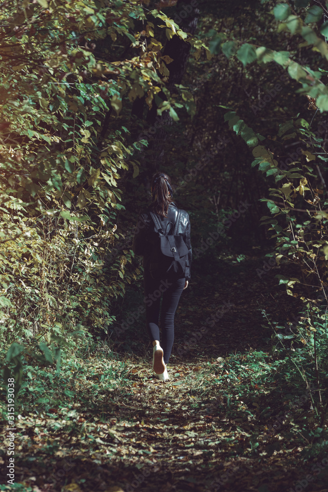Lonely girl walking in the autumn forest. Vertical frame, back view Lonely girl walking in the autumn forest. Vertical frame, back view