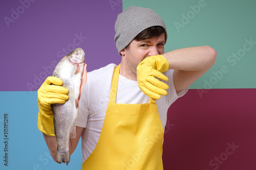 Vászonkép Young caucasian fisher holding a rotten fish isolated on colored background