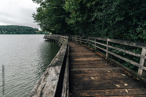 Wooden walkway or bridge on the side of a lake. Old wooden walkway on the banks of a lake. Autumn view of a wooden path and a lake.