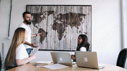 A person is pointing on a map. People are in the office. They are planing a business trip.