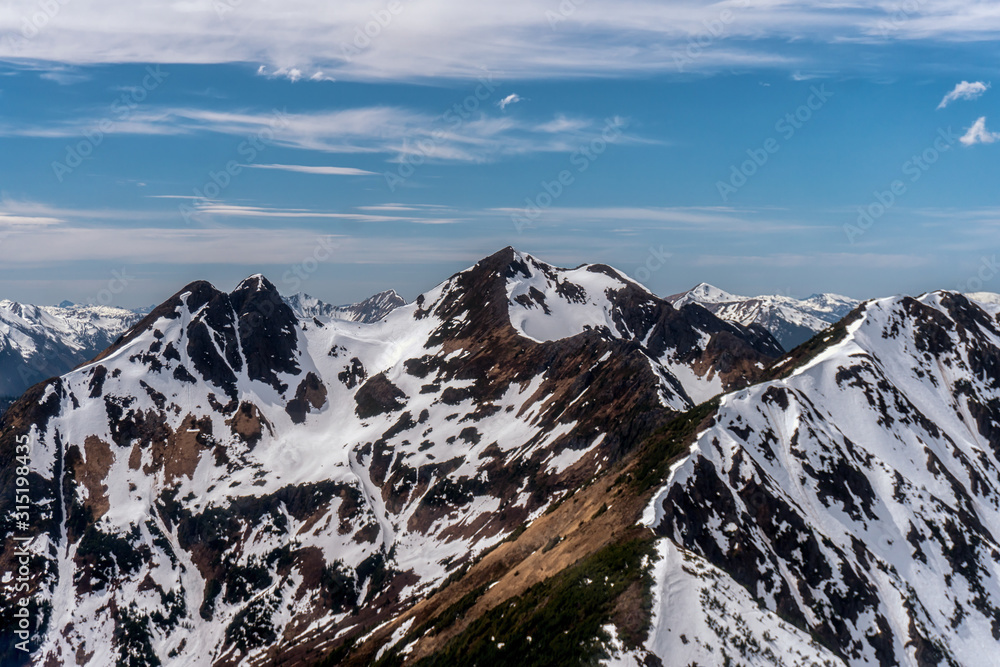 Obraz premium Amazing mountain peaks covered with snow. Beautiful clouds are on a background. Flight seeing tour by helicopter in Alaska. 