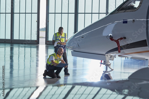Air traffic control ground crew workers examining corporate jet in airplane hangar