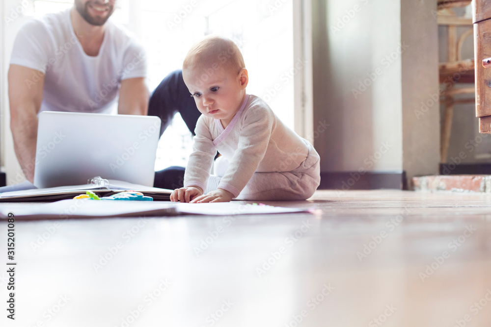 Baby girl playing on floor near father working at laptop Baby girl playing on floor near father working at laptop
