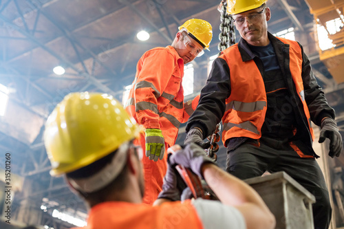 Steel workers fastening crane hook to steel in factory