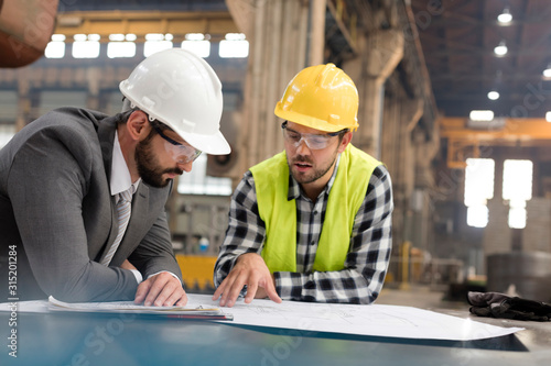 Manager and engineer reviewing blueprints in steel factory photo
