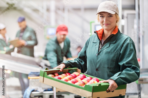 Portrait confident female worker carrying box of apples in food processing plant