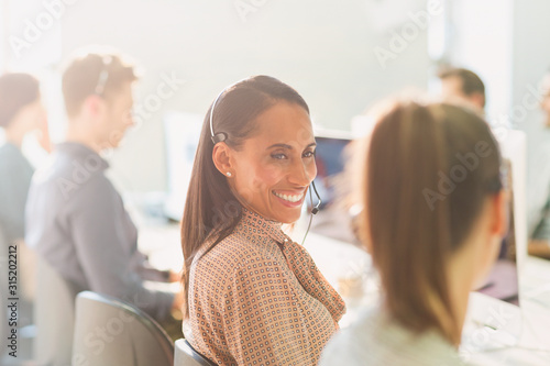 Smiling female telemarketers wearing headsets talking in sunny office photo