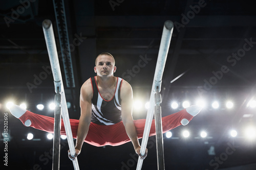 Male gymnast performing splits on parallel bars photo