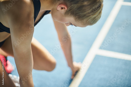 Focused female runner ready at starting block on sports track photo