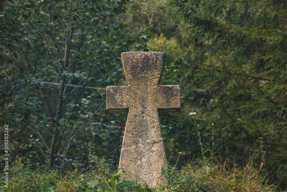 stone concrete cross religion sigh on ground hill with forest spruce needle trees dark green moody foliage unfocused background