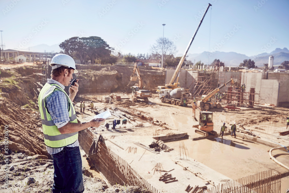Construction worker foreman using walkie-talkie at sunny construction site Construction worker foreman using walkie-talkie at sunny construction site