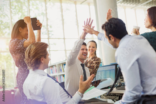 Business people high-fiving and celebrating in office