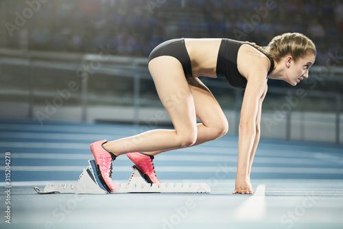 Focused female runner ready at starting block on sports track