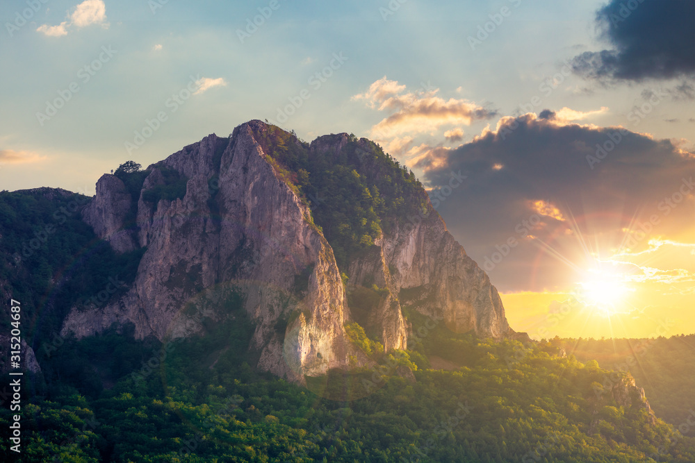 rock formation on the field at sunset. beautiful rural landscape in mountains. wonderful scenery in spring. clouds on the blue sky in evening light. forest on the hills