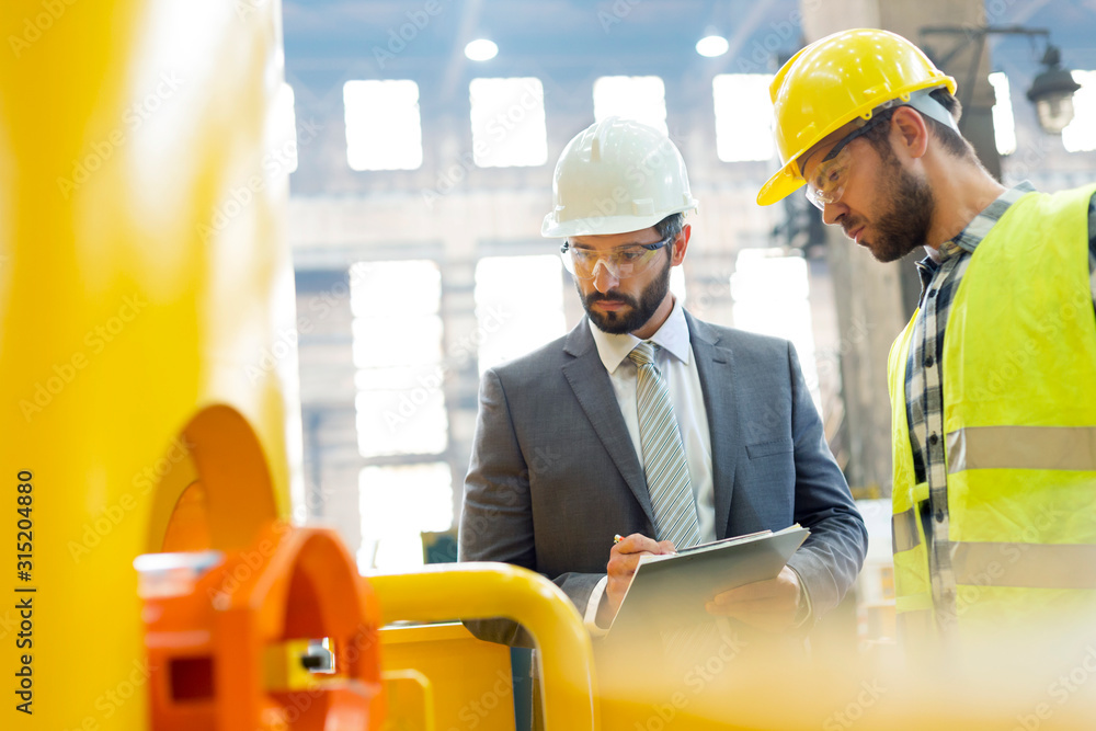 © Rafal Rodzoch/Caia Image - Manager and steel worker examining equipment in factory