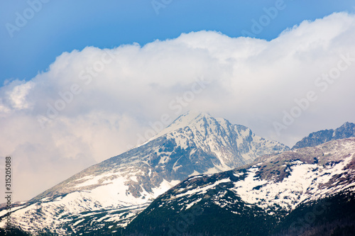 high tatras mountain ridge in springtime. snow capped rocky peaks in dramatic dappled sunlight beneath a clouds on a blue sky. place where earth meets sky concept © Pellinni