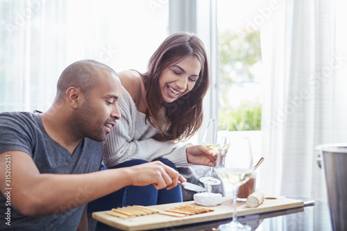 Smiling couple drinking white wine eating crackers cheese in living room