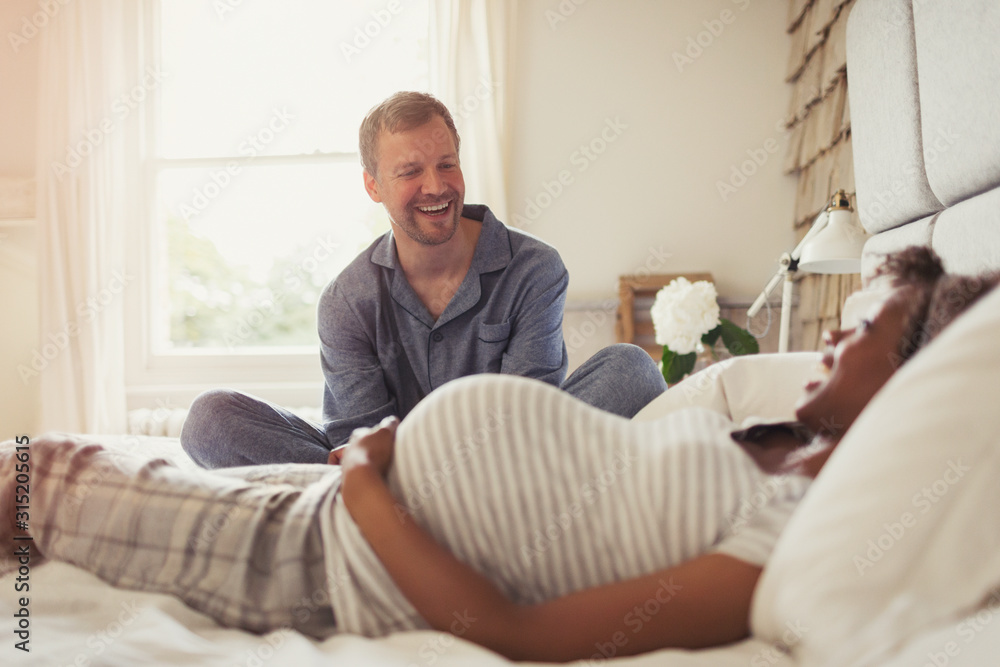 Multi-ethnic pregnant couple relaxing and laughing on bed Multi-ethnic pregnant couple relaxing and laughing on bed