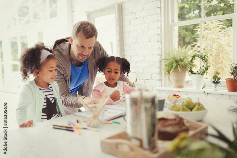 Multi-ethnic father and daughters coloring in kitchen Multi-ethnic father and daughters coloring in kitchen