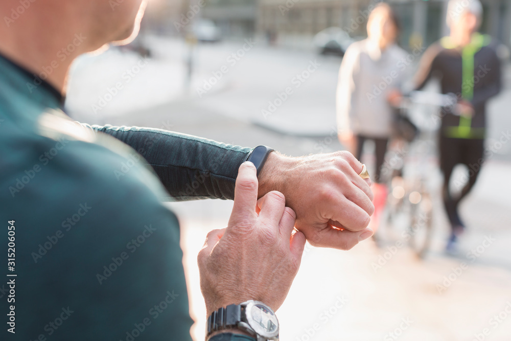Male runner checking smart watch on urban sidewalk Male runner checking smart watch on urban sidewalk