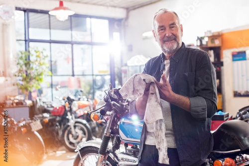 Portrait smiling senior male motorcycle mechanic wiping hands on rag in workshop