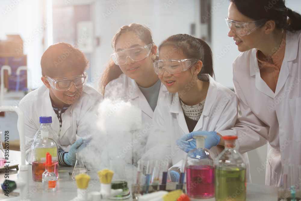 Female teacher and students watching scientific experiment chemical reaction in laboratory classroom Female teacher and students watching scientific experiment chemical reaction in laboratory classroom