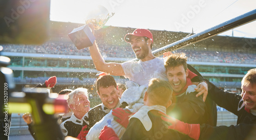 Formula one racing team carrying driver trophy on shoulders, celebrating victory