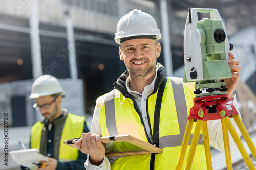 Portrait smiling male engineer using theodolite at construction site photo