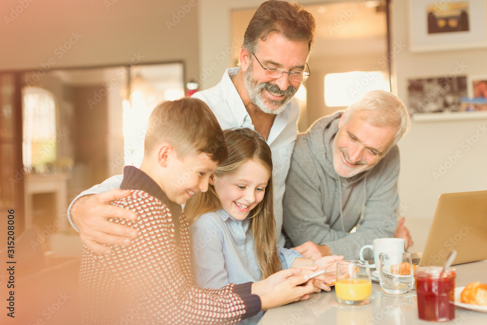 Male gay parents and children using cell phone at kitchen counter Male gay parents and children using cell phone at kitchen counter