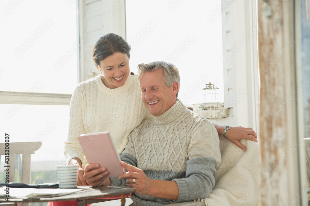 Smiling mature couple using digital tablet at table on sunny sun porch Smiling mature couple using digital tablet at table on sunny sun porch