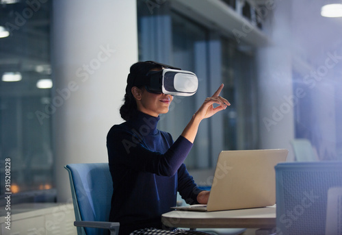 Businesswoman using virtual reality simulator at laptop in office photo