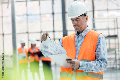 Male engineer reviewing blueprints on clipboard at construction site photo