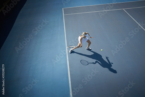 Overhead view young female tennis player playing tennis, hitting the ball on sunny blue tennis court