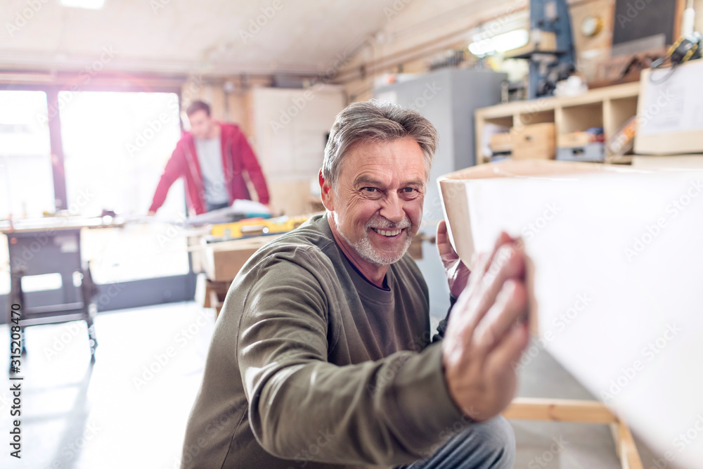 Smiling male carpenter examining wood boat in workshop Smiling male carpenter examining wood boat in workshop