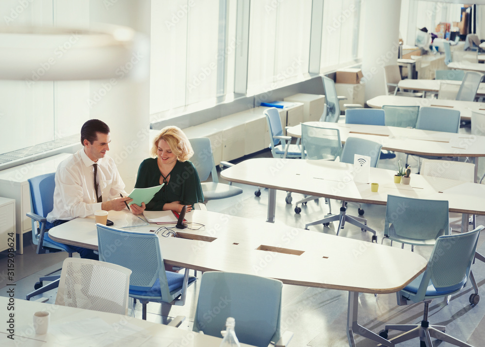 Businessman businesswoman discussing paperwork at table in shared workspace Businessman businesswoman discussing paperwork at table in shared workspace