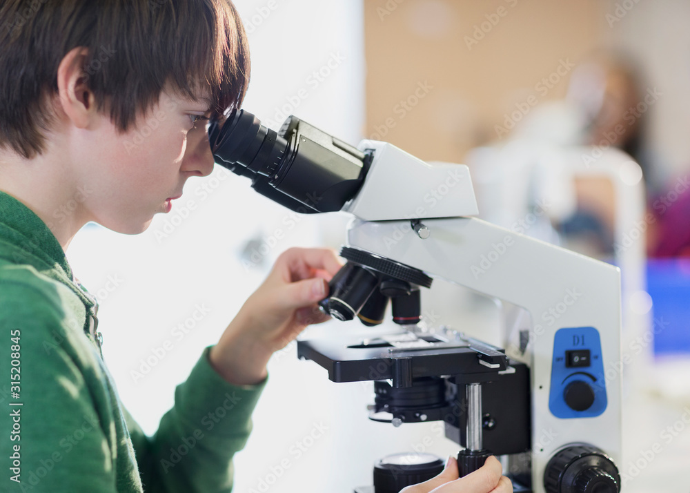 Focused boy student using microscope in classroom Focused boy student using microscope in classroom