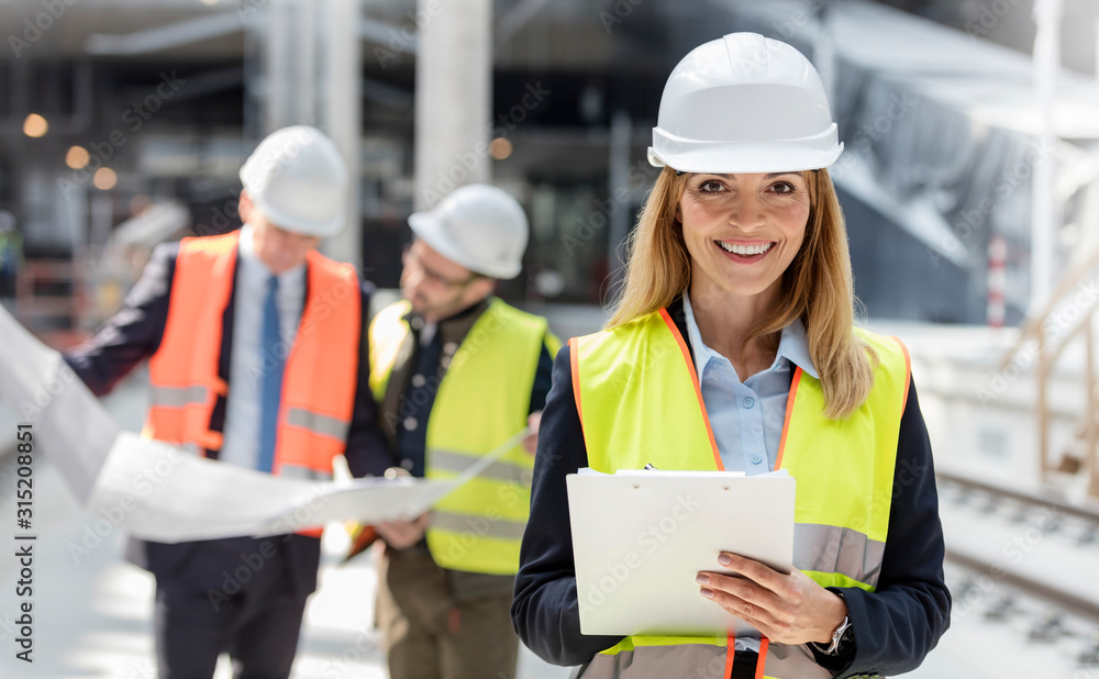 Portrait smiling female engineer with clipboard at construction site Portrait smiling female engineer with clipboard at construction site
