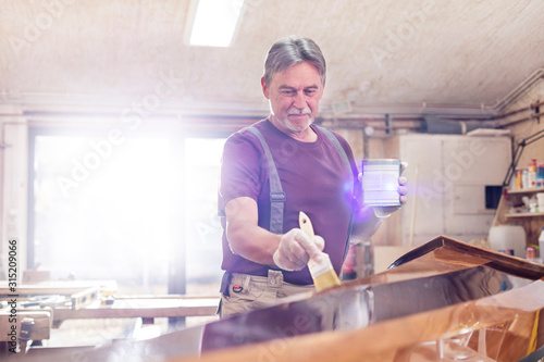 Male carpenter staining wood kayak in workshop