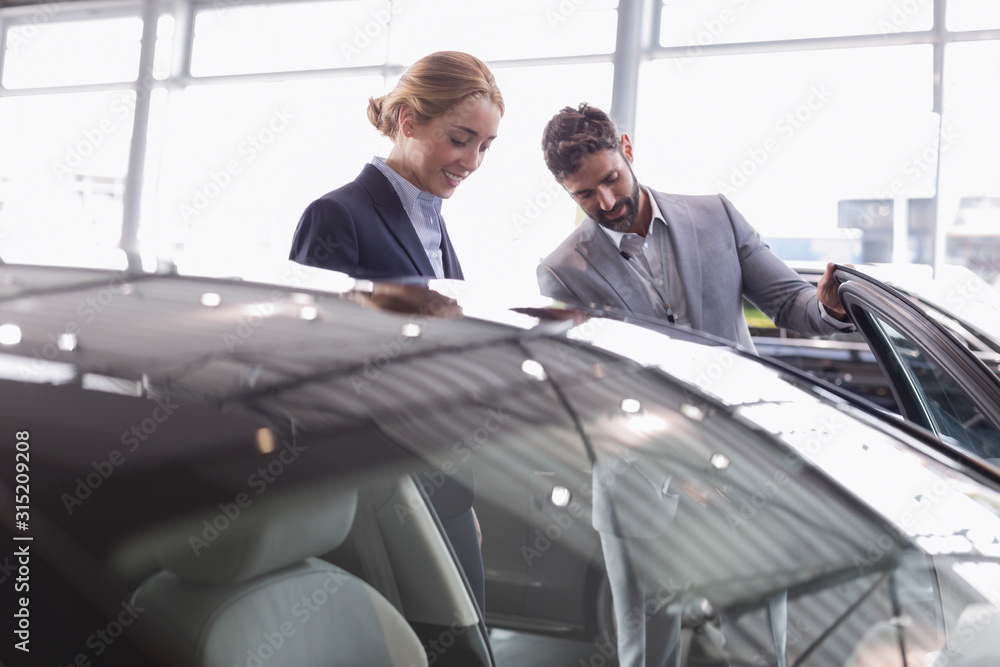 Car salesman showing new car to female customer in car dealership showroom Car salesman showing new car to female customer in car dealership showroom