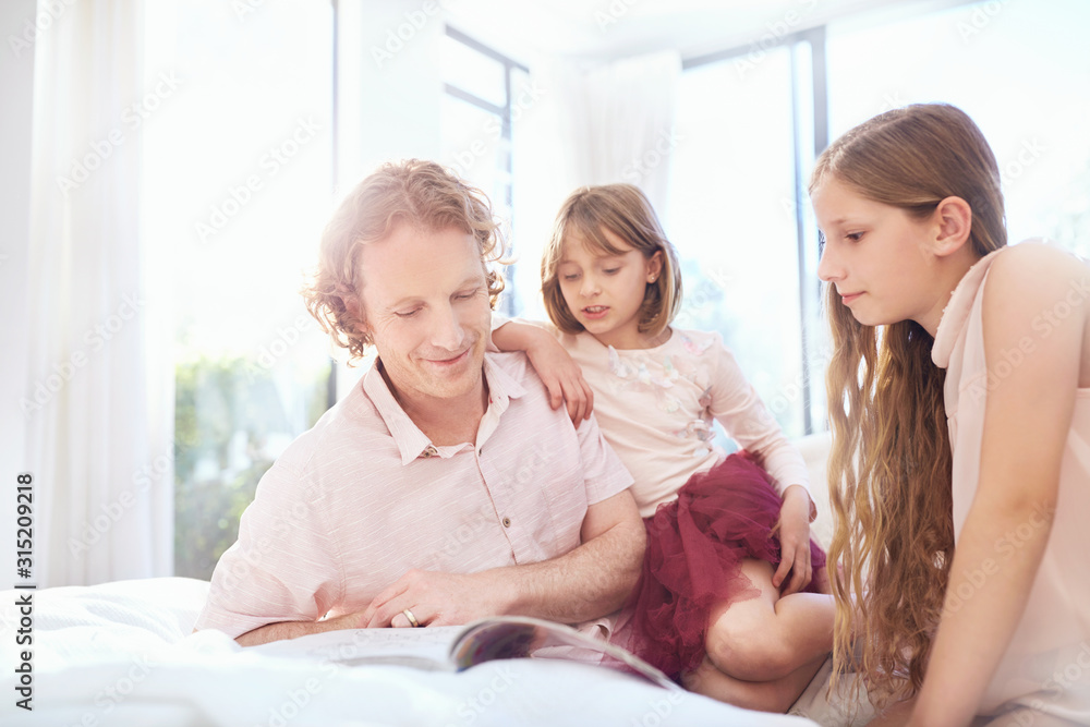 Father and daughters reading book on bed Father and daughters reading book on bed