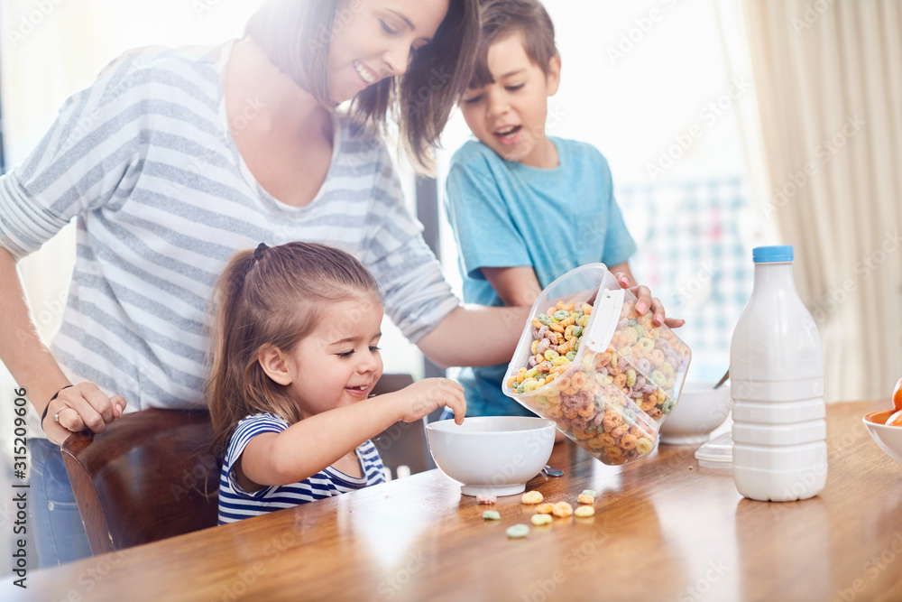 Mother pouring cereal for daughter at breakfast table Mother pouring cereal for daughter at breakfast table