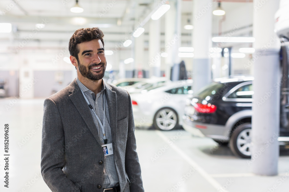 Portrait smiling car salesman looking away in car dealership auto repair shop Portrait smiling car salesman looking away in car dealership auto repair shop